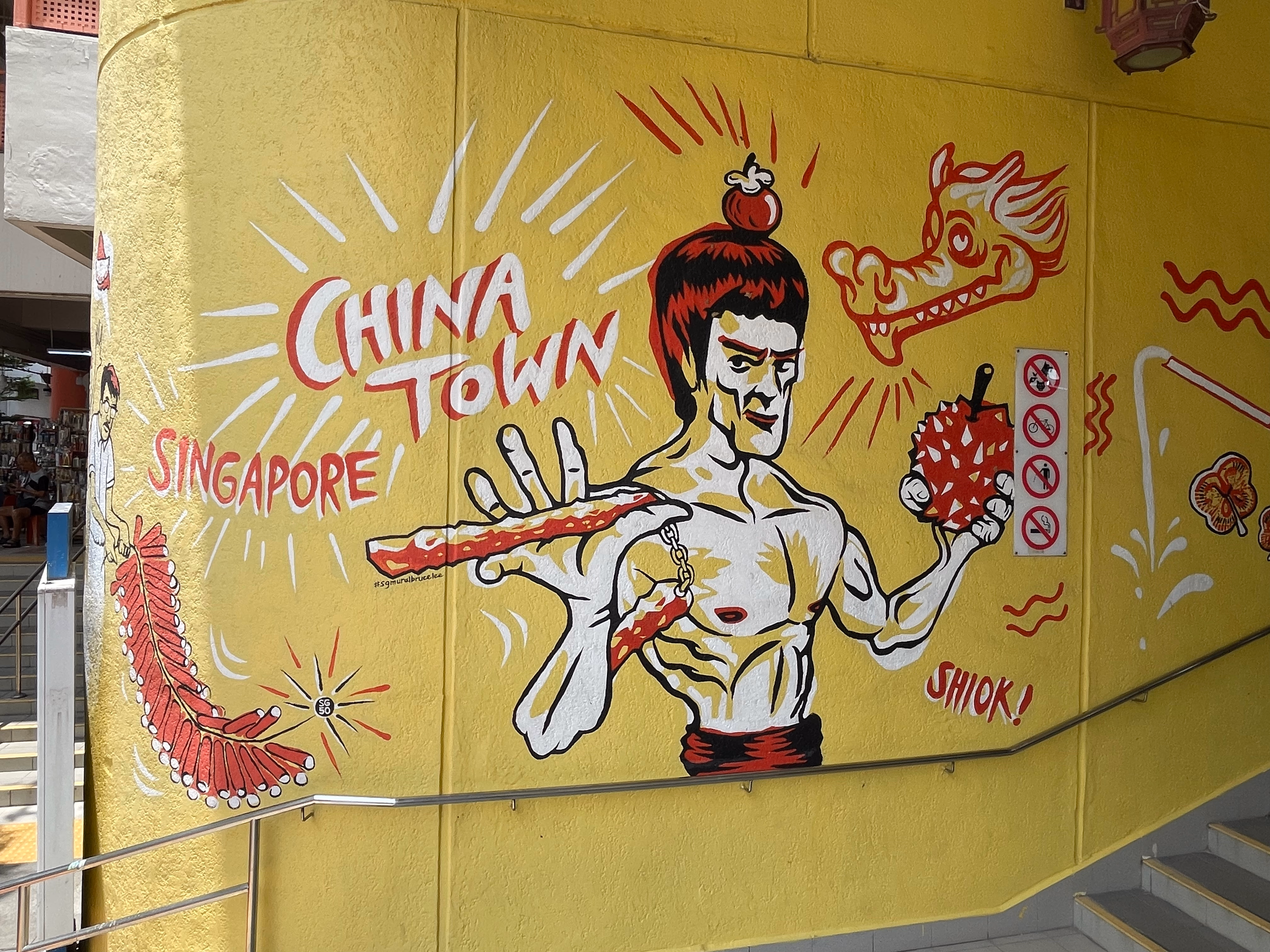 A yellow wall mural reading Chinatown Singapore with a martial artist holding a lantern.
