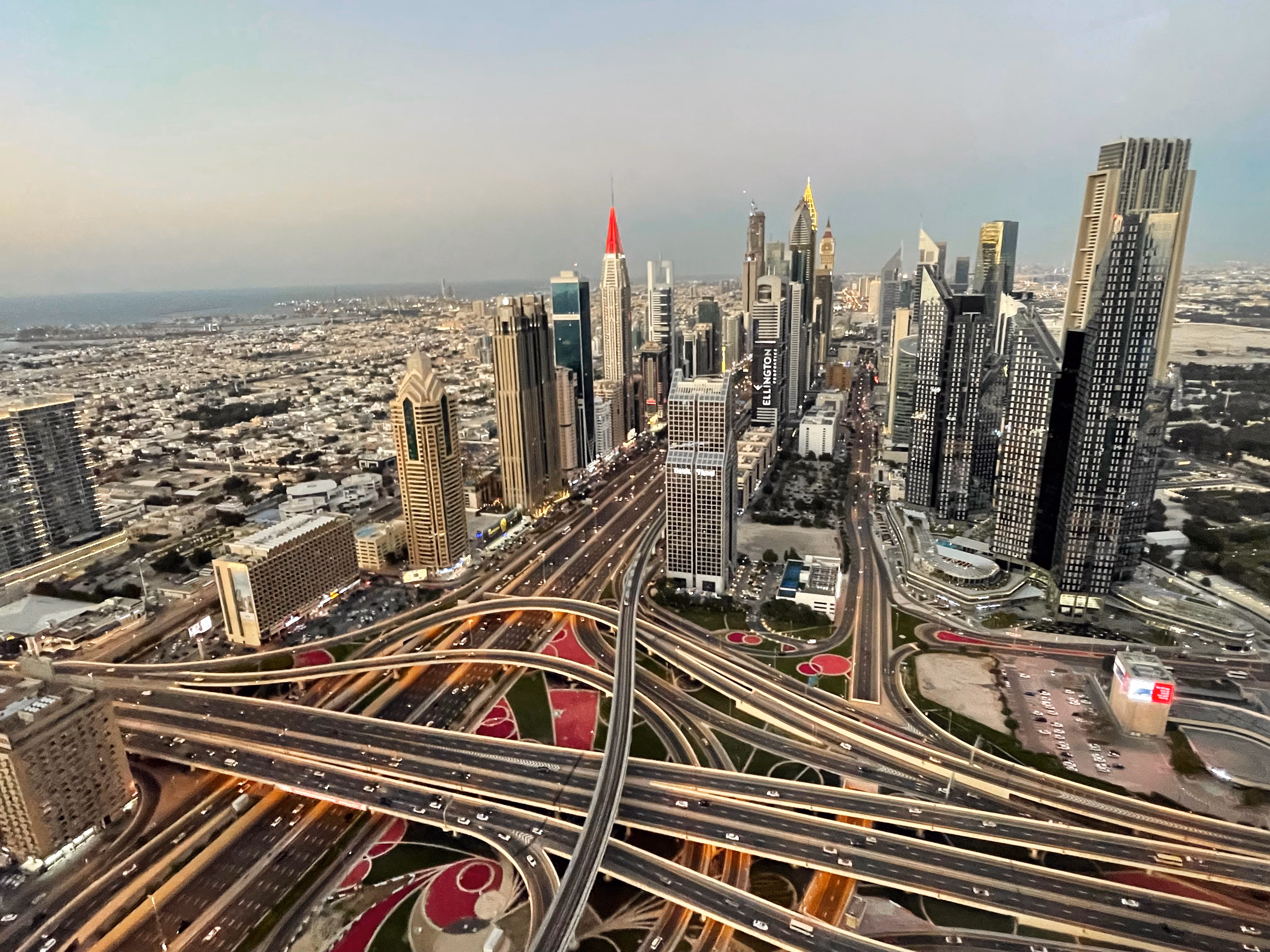 Sheikh Zayed Road at dawn — a row of glass towers above a multi-level interchange, the city stretching toward the hazy coast.