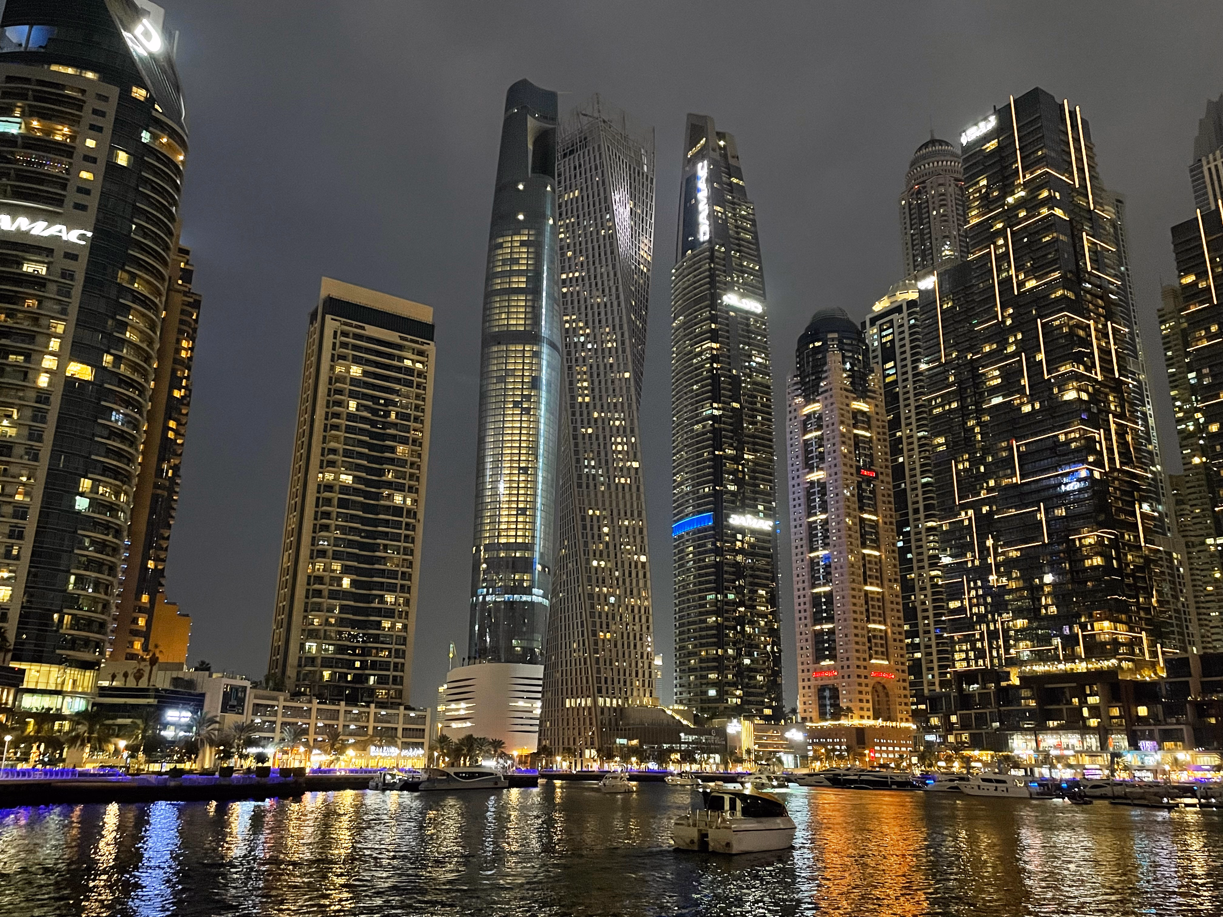 The Marina at night — the twisting Cayan Tower and its neighbours blazing with window light, mirrored on the water below.