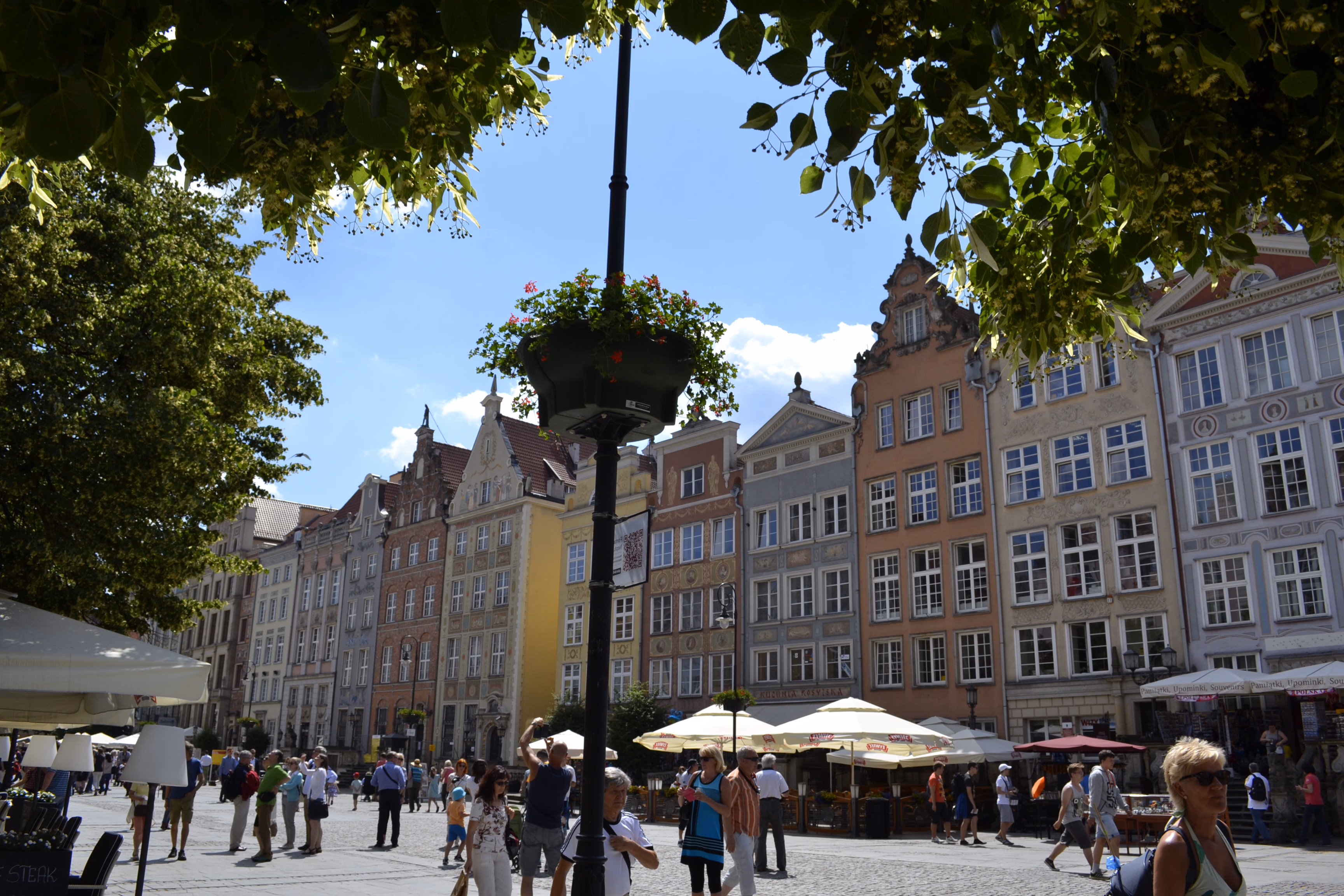 Gdańsk's Long Market — narrow Hanseatic townhouses in yellow, terracotta and grey, each with a different carved gable and café terrace below.