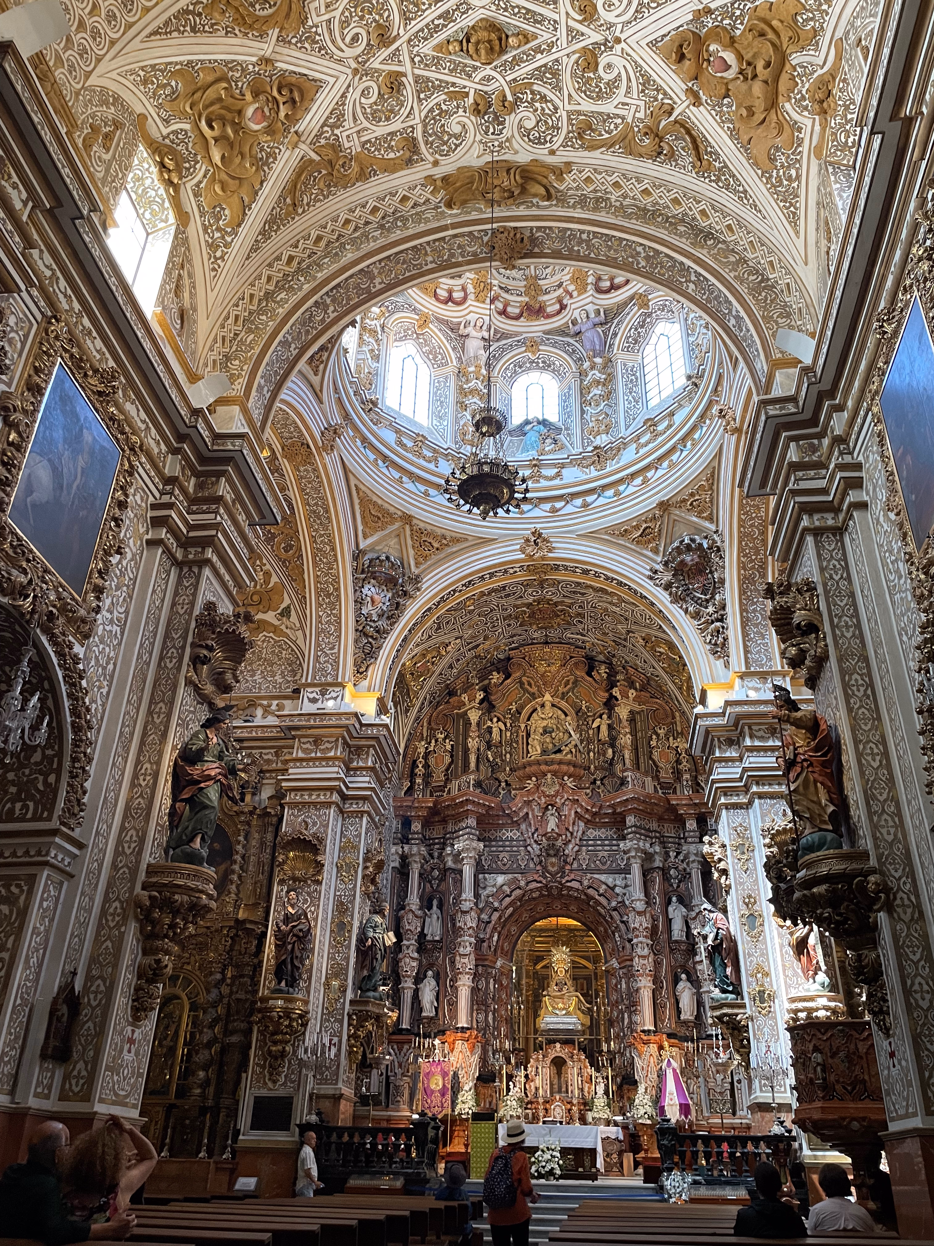 The nave of the Basilica of San Juan de Dios — gold filigree on white vaults, a carved wooden retablo and daylight falling through the dome.