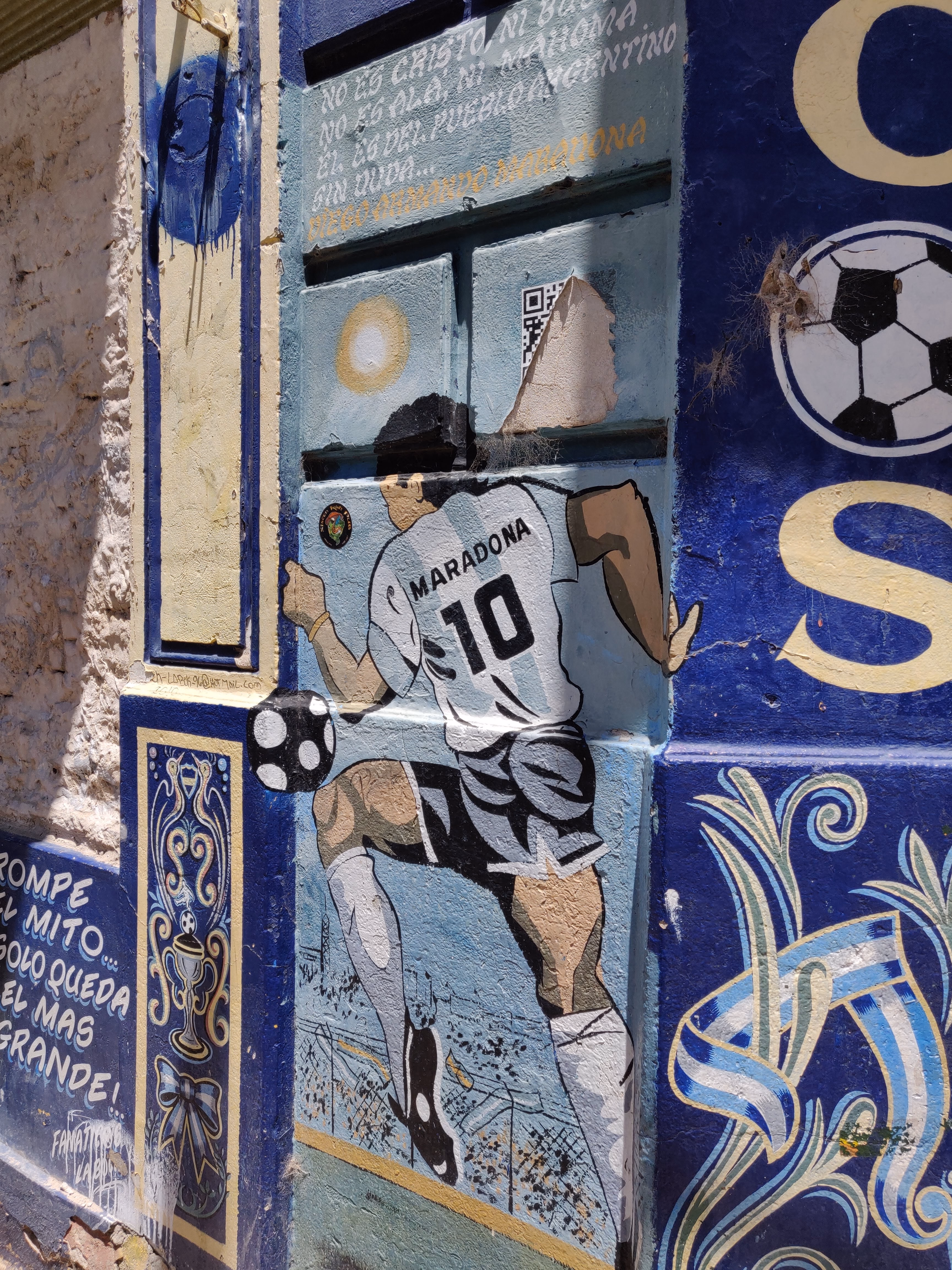 Maradona juggles a ball on a royal-blue mural framed in fileteado scrollwork — a poem above reads "Él es del pueblo argentino... Diego Armando Maradona."