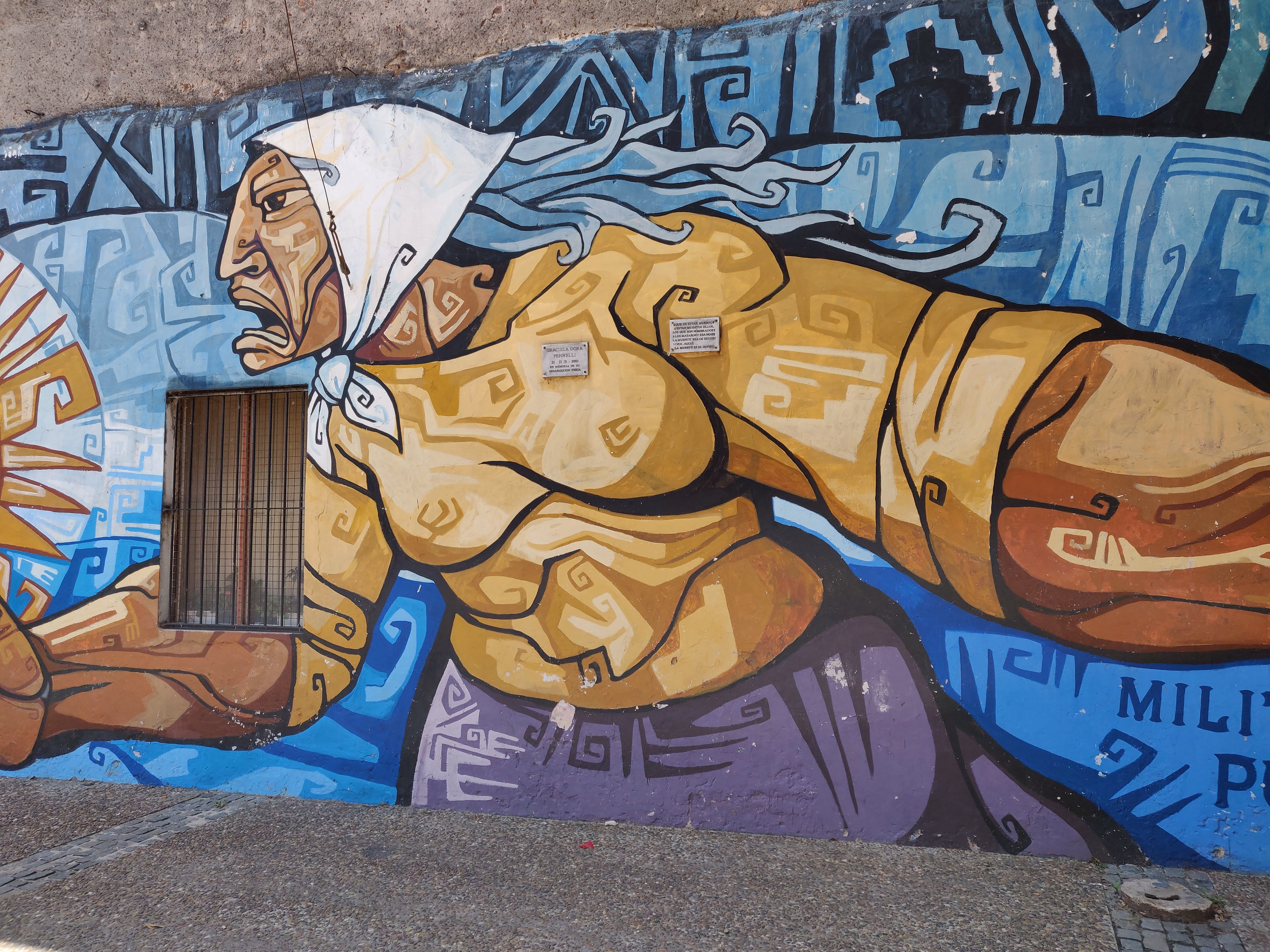 A woman lunges forward on a stone wall, hair streaming in blue waves — golden skin, geometric tattoos and a stylised sun behind her outstretched arm.