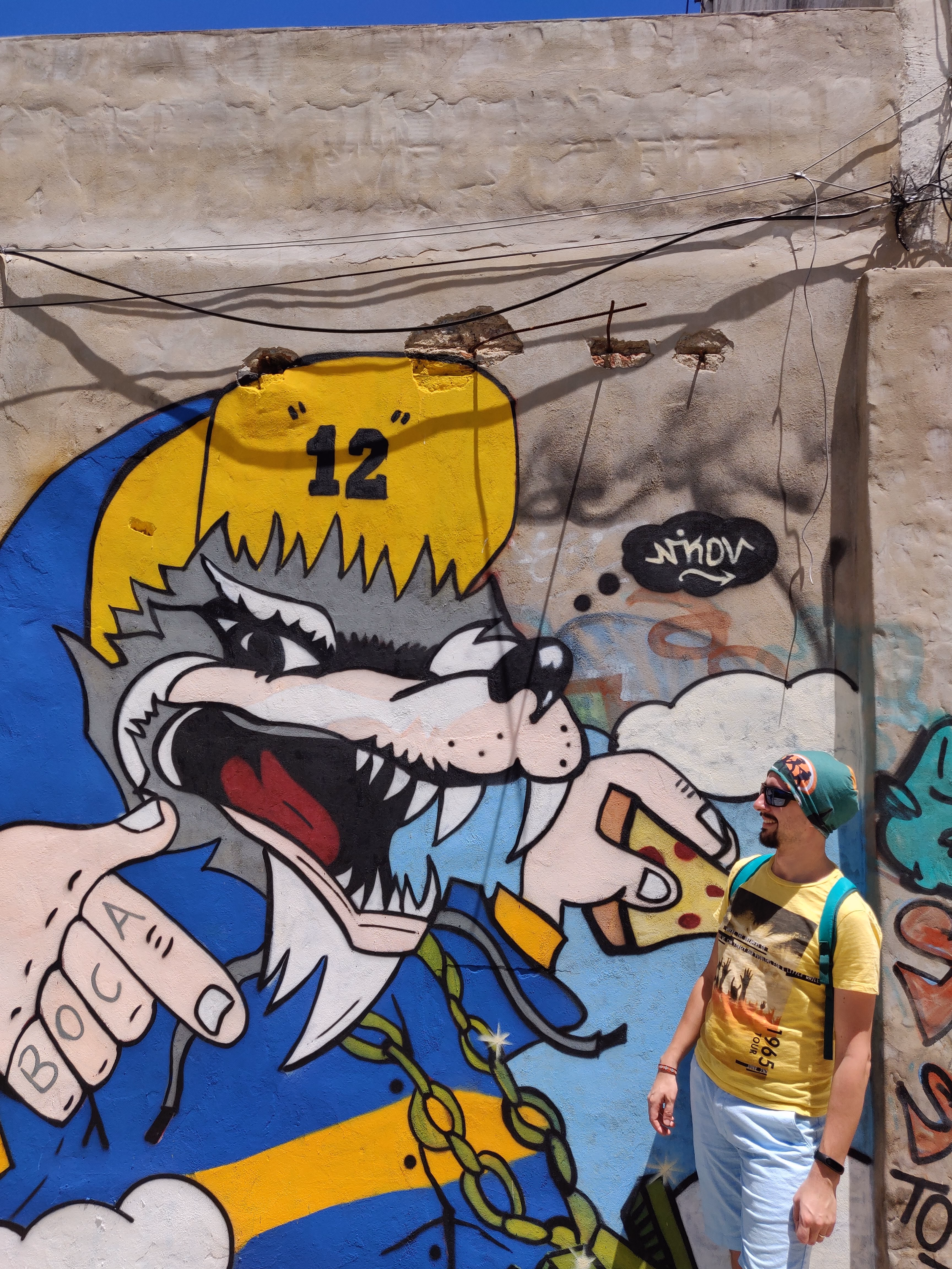 A snarling wolf in Boca blue and yellow holds a slice of pizza — "BOCA" tattooed across its knuckles and a number 12 cap for La Doce, the club's ultras.
