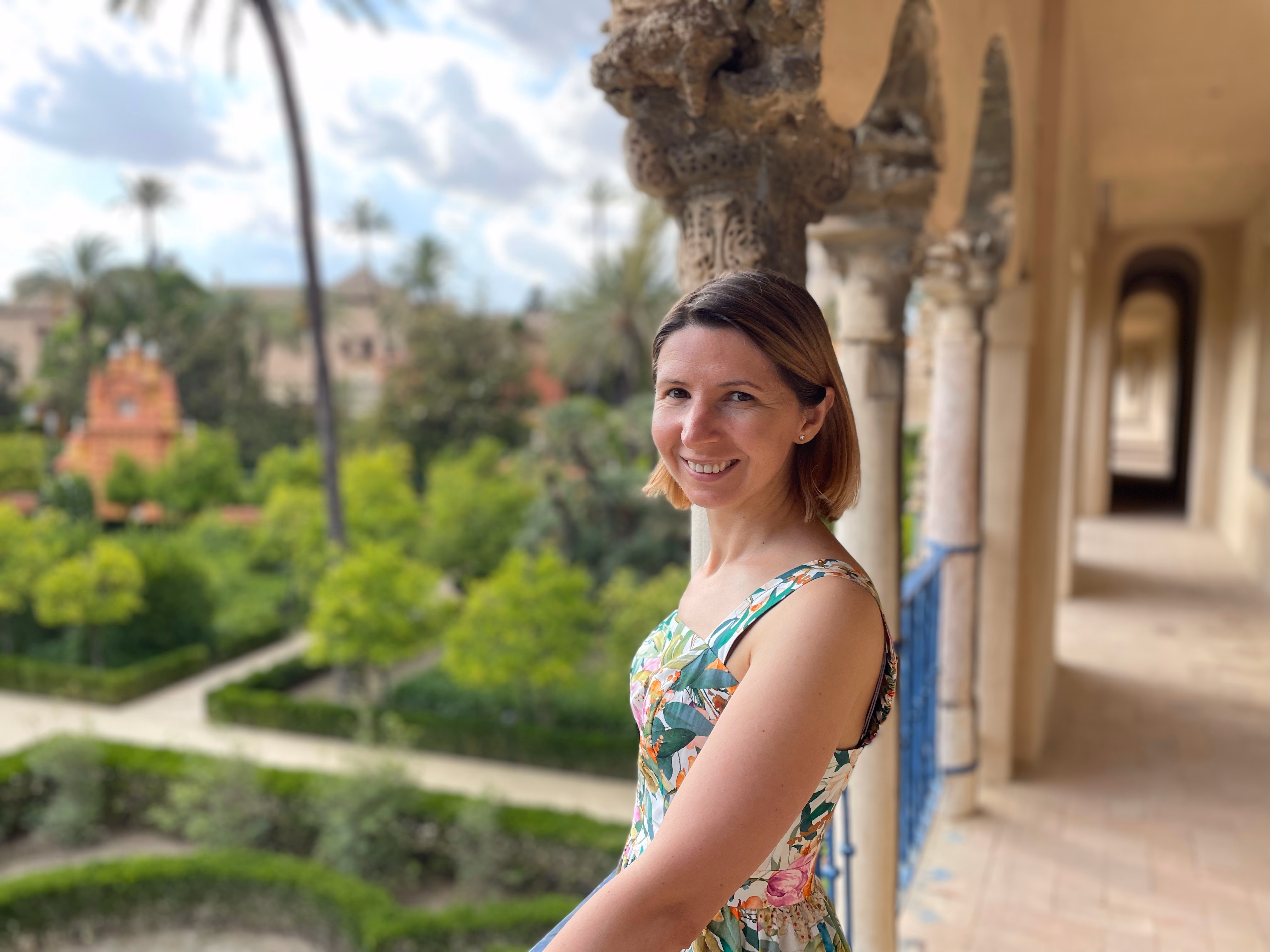 Ornate stone arches overlooking the Alcázar gardens — palms, clipped hedges and terracotta rooftops below.