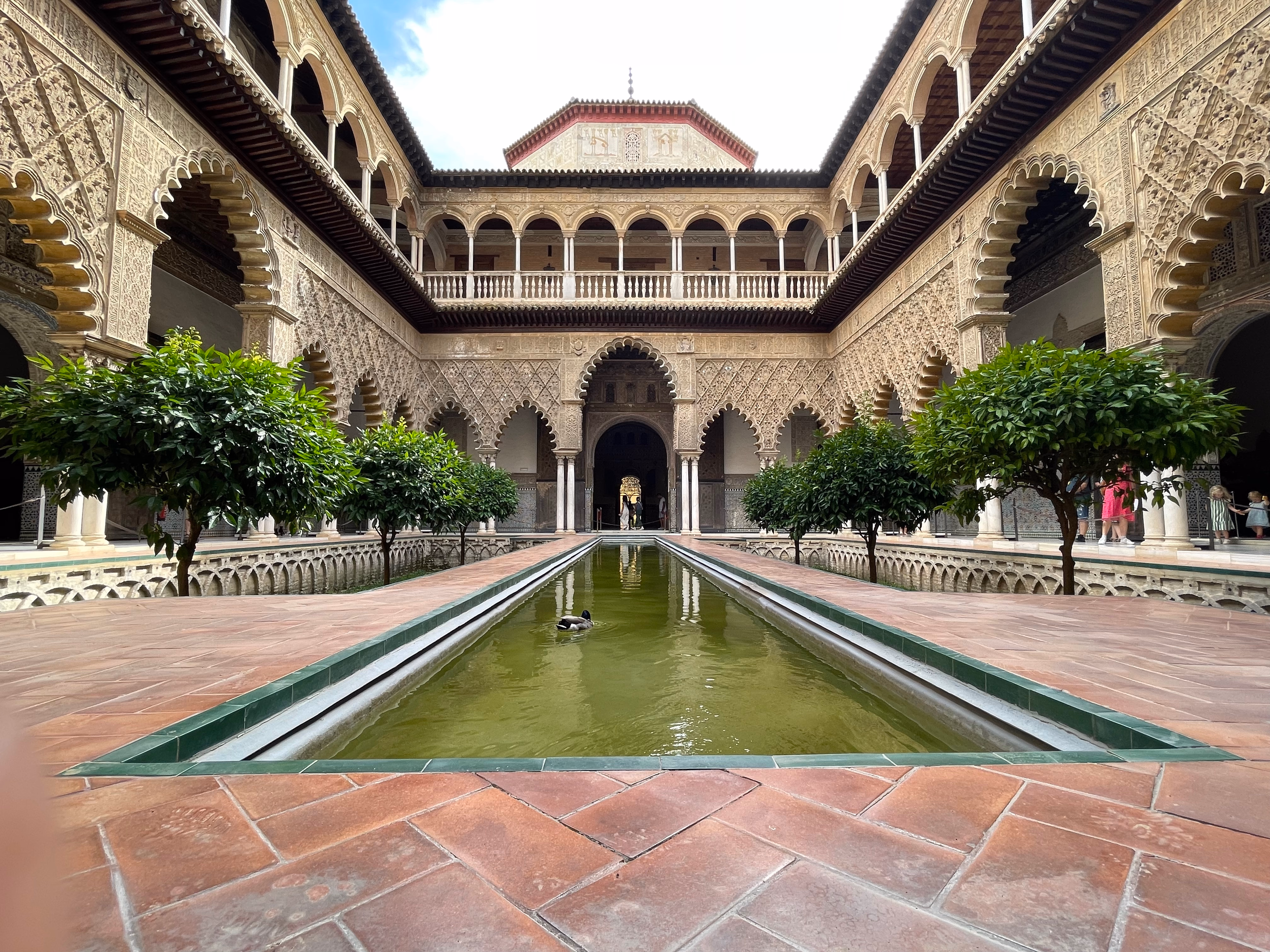 The Patio de las Doncellas at the Real Alcázar — a long reflecting pool lined with orange trees and lace-like Mudéjar arches.