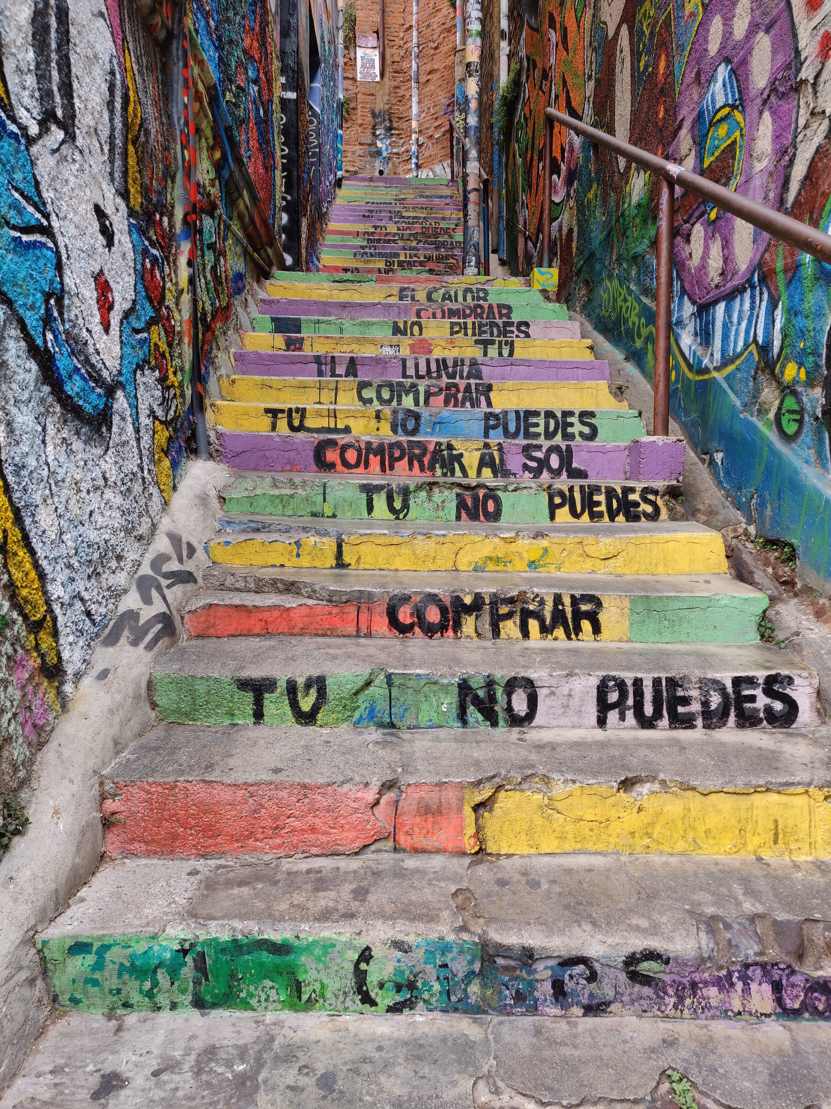 A narrow stairway painted in yellow, green and red — each riser stencilled with a line from Calle 13's "Latinoamérica," walls layered in graffiti on both sides.